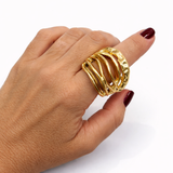 Anel dourado oval com faixas onduladas e textura trabalhada, no dedo