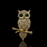 Broche de coruja dourada com olhos verdes e cristais brilhantes, detalhes em strass