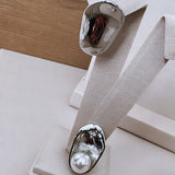 Brincos prateados em formato oval com detalhe côncavo e brilho espelhado