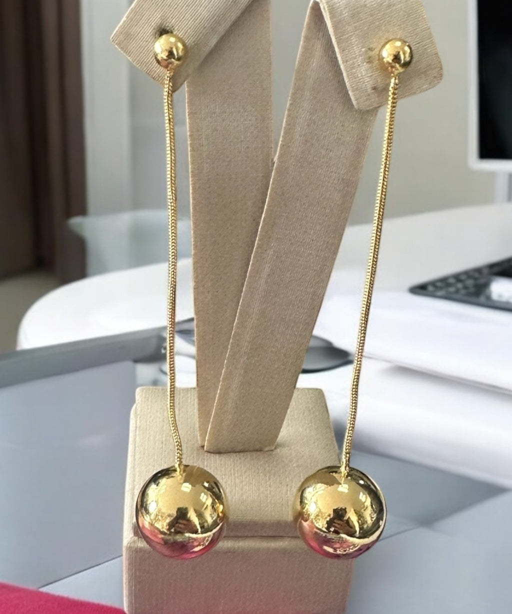 Brinco longo de esfera grande com hastes finas e banho dourado, em suporte