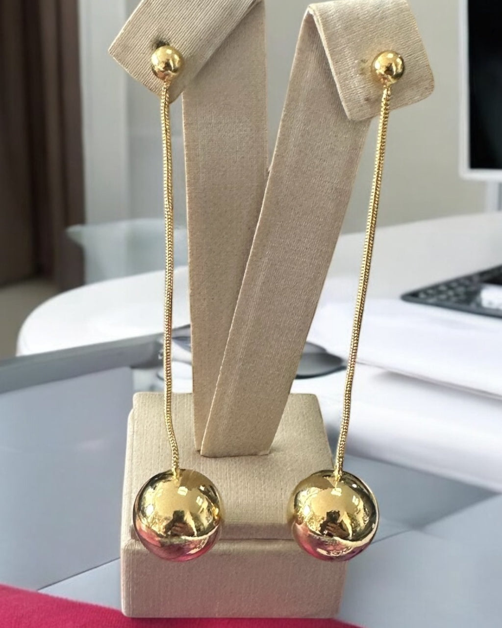 Brinco longo de esfera grande com hastes finas e banho dourado, em suporte