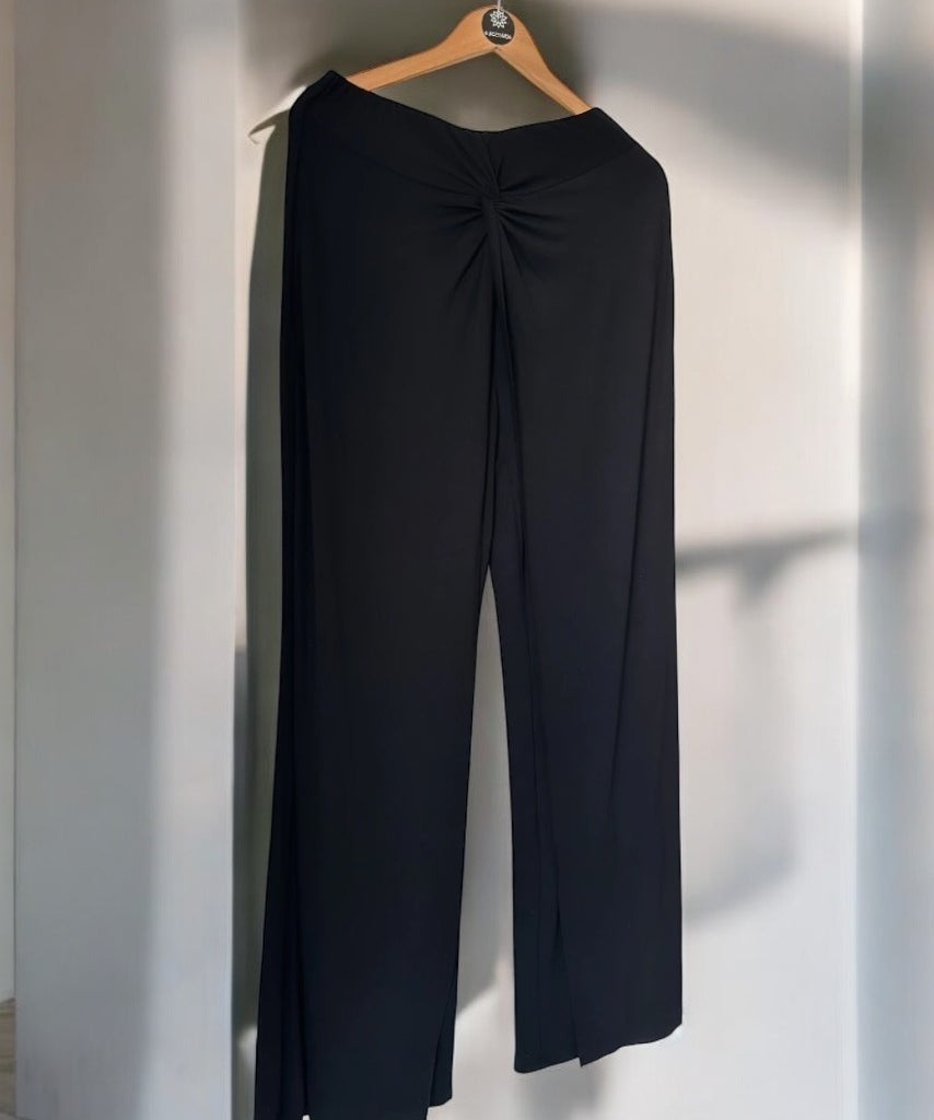 Calça pantalona preta com pregas no cós e pernas largas, vista traseira.