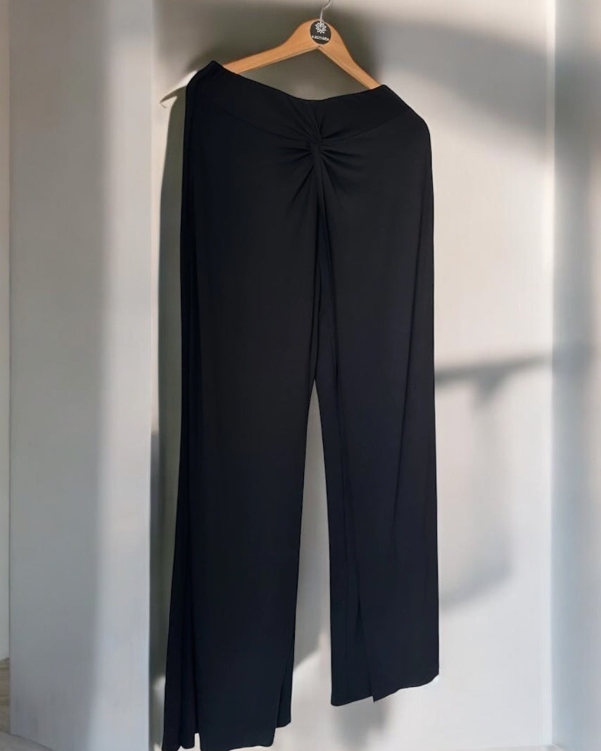Calça pantalona preta com pregas no cós e pernas largas, vista traseira.