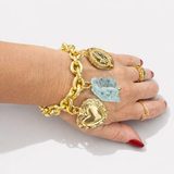Pulseira Maria Liana dourada com elos e pingentes, incluindo medalha e pedra azul-clara.