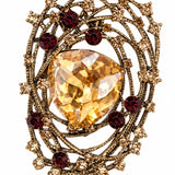 Broche metal dourado com pedra oval amarela e cristais vermelhos ao redor