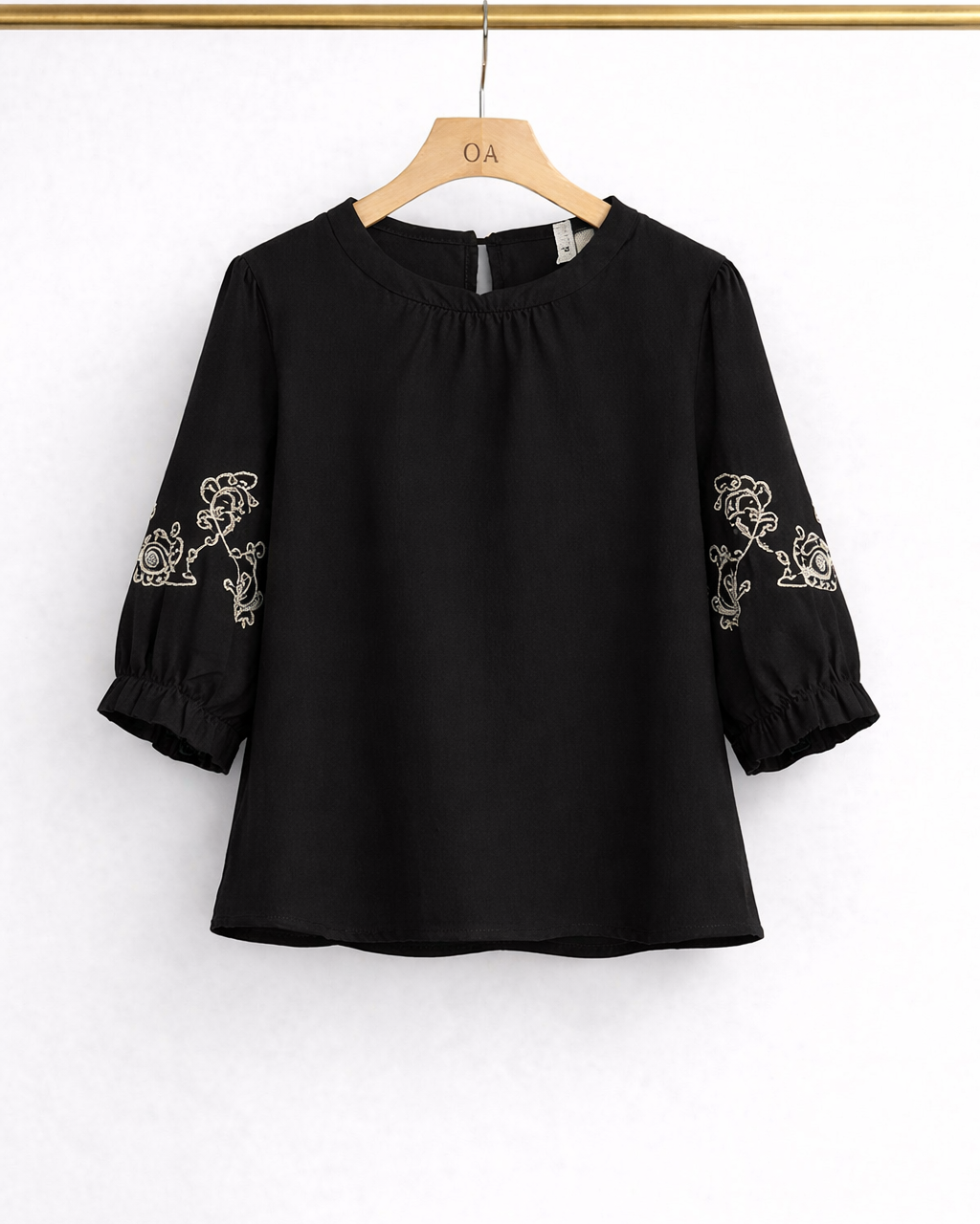 Blusa preta de gola franzida e bordado branco nas mangas bufantes, vista frontal