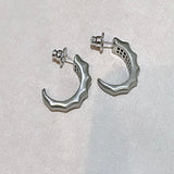 Par de brincos prateados em meia-lua com detalhe de onda, com tarraxa.