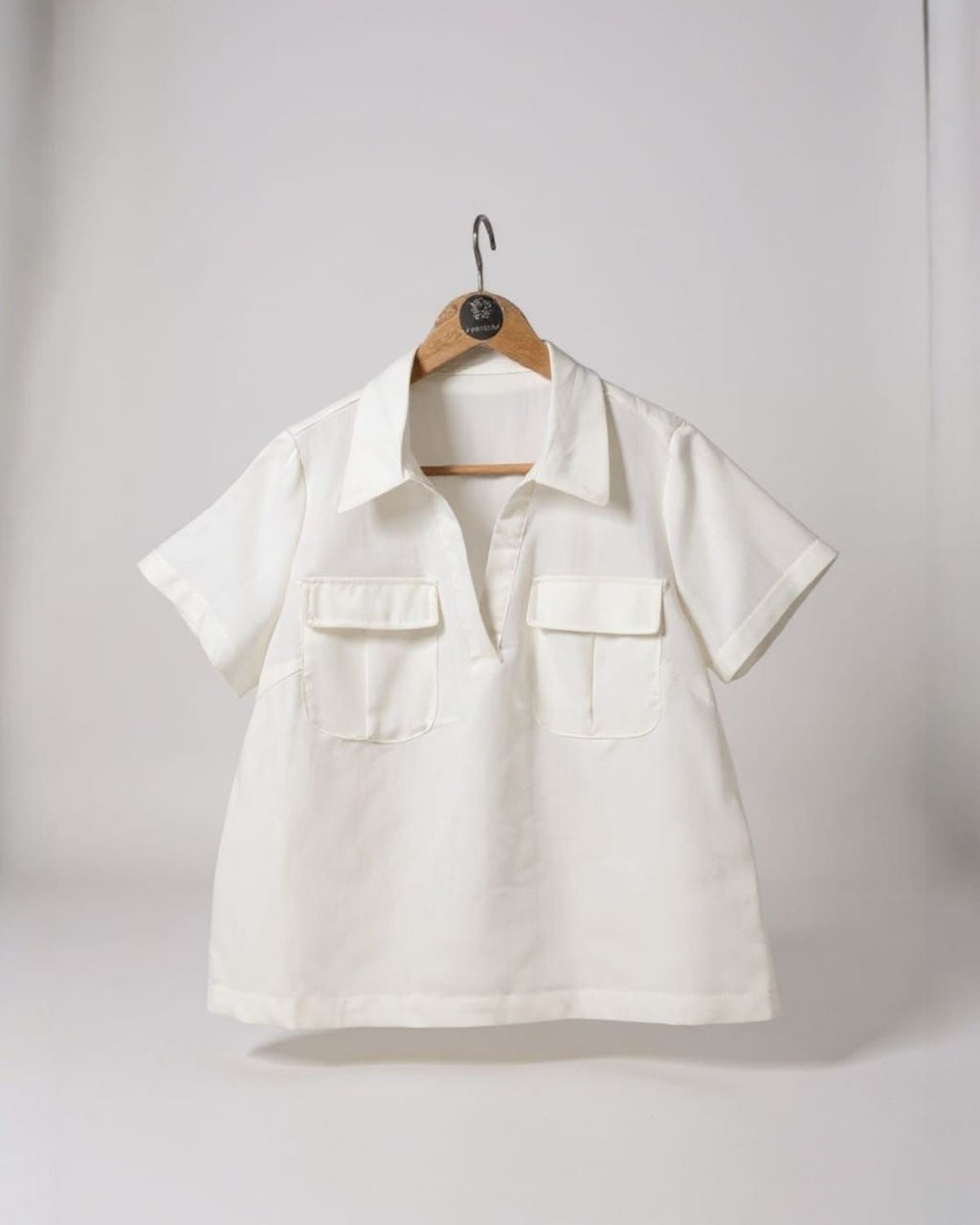 Blusa branca em cabide, gola polo, botões frontais e mangas curtas com bolsos