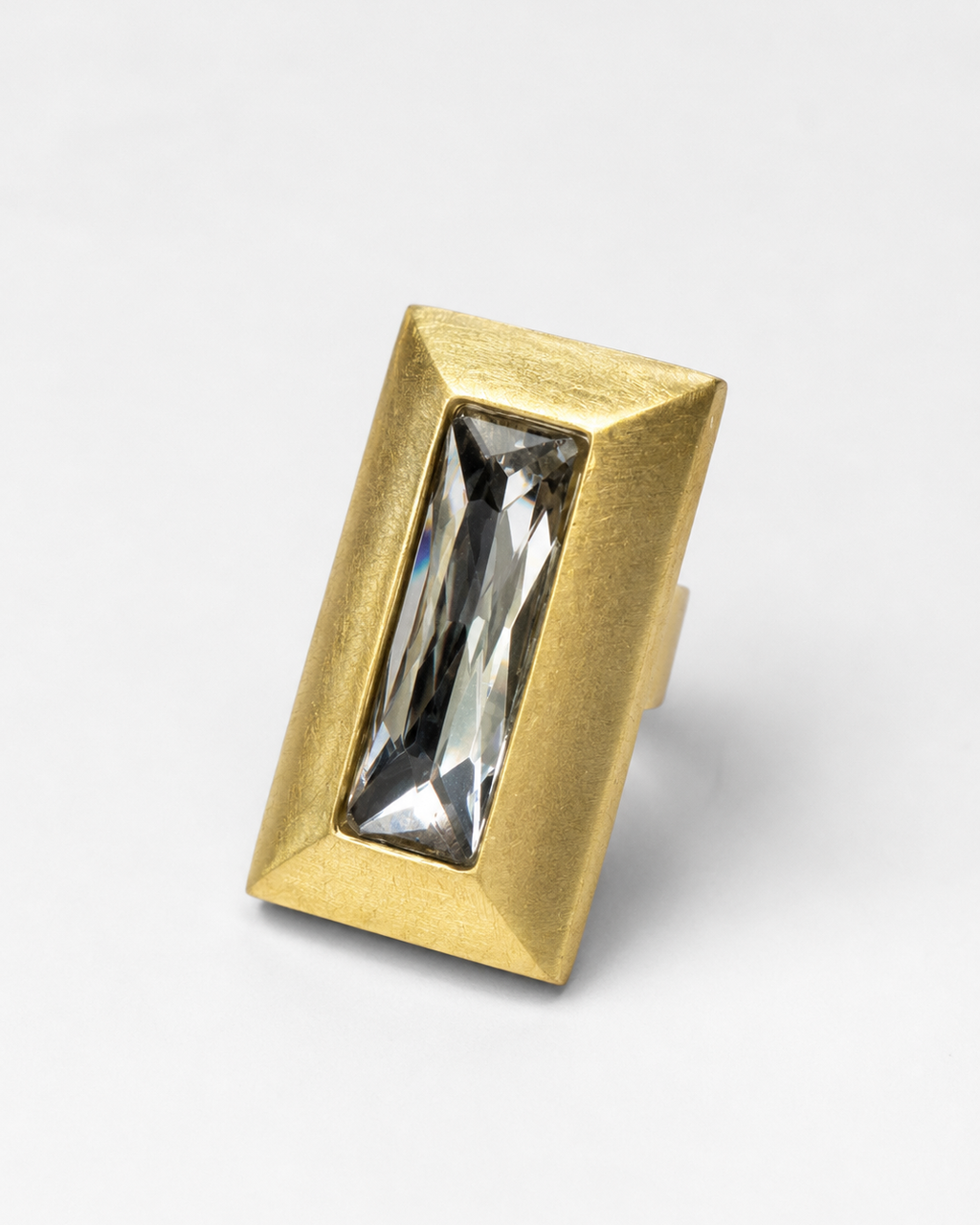 Anel retangular dourado com pedra central transparente e borda texturizada