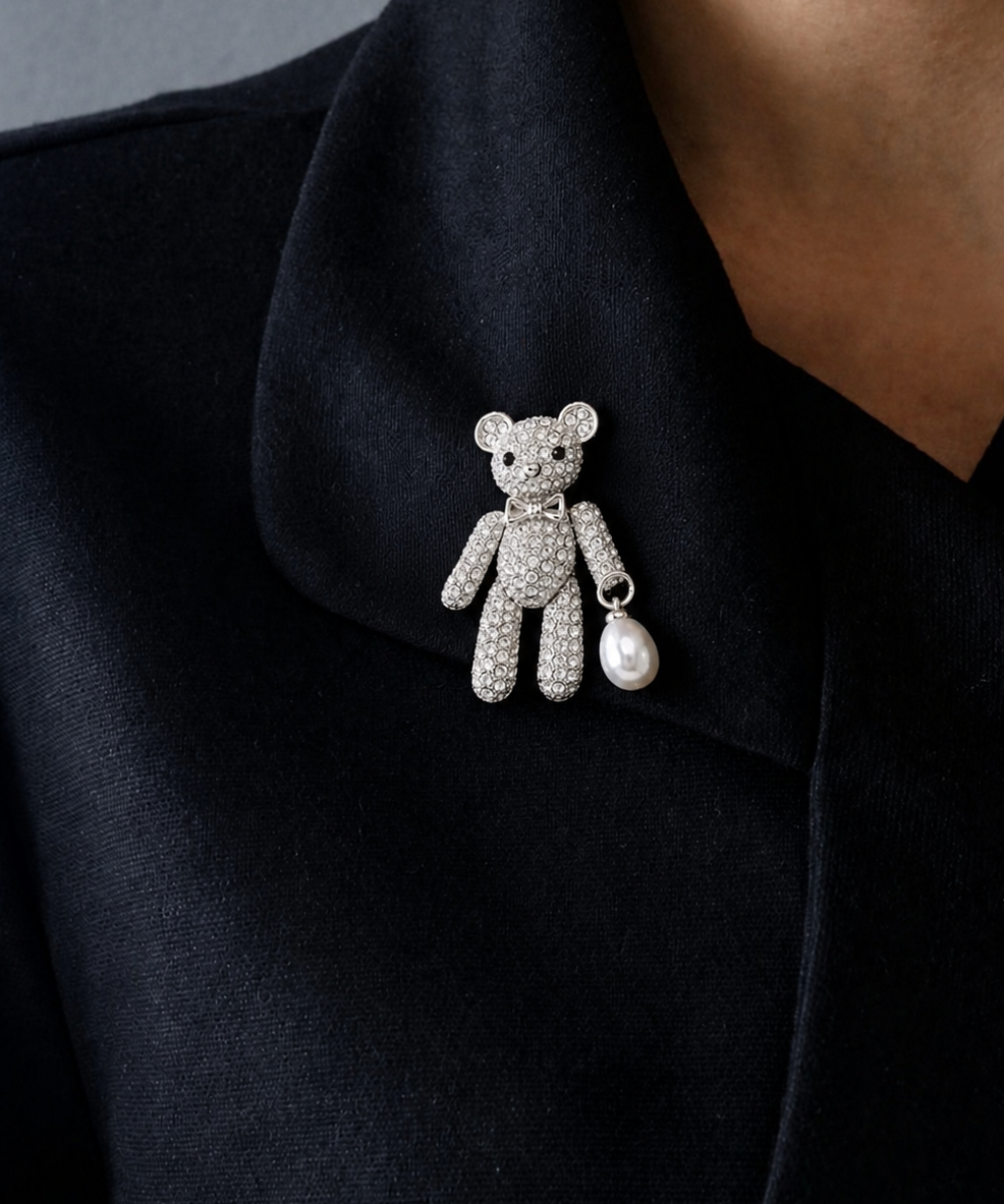 Broche de ursinho prateado com strass e pérola pendente na lapela