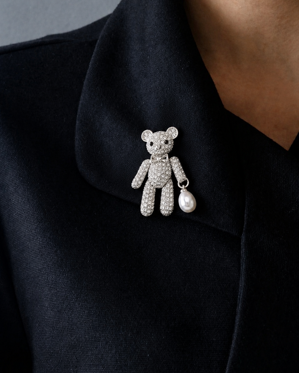Broche de ursinho prateado com strass e pérola pendente na lapela