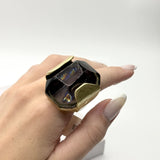 Anel com pedra escura e aro dourado quadrado com brilho multicolor