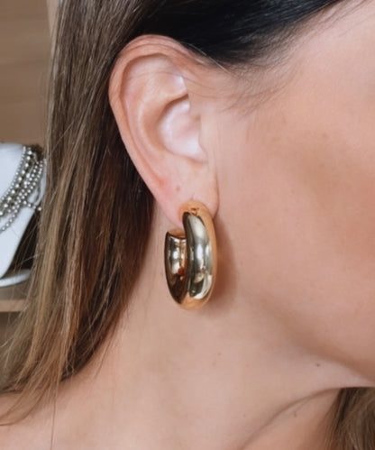 Brinco de argola dourada oval com detalhes brilhantes, em vista lateral
