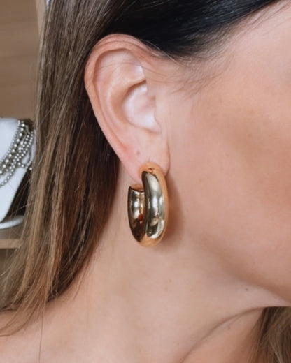 Brinco de argola dourada oval com detalhes brilhantes, em vista lateral