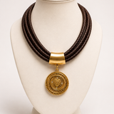 Colar Trevis Gold com cordão trançado escuro e pingente circular com brasão dourado
