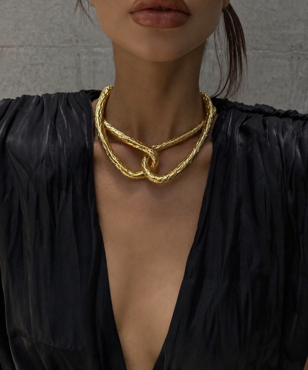 Colar Romina dourado com elos curvos e trançados, sobreposto no pescoço