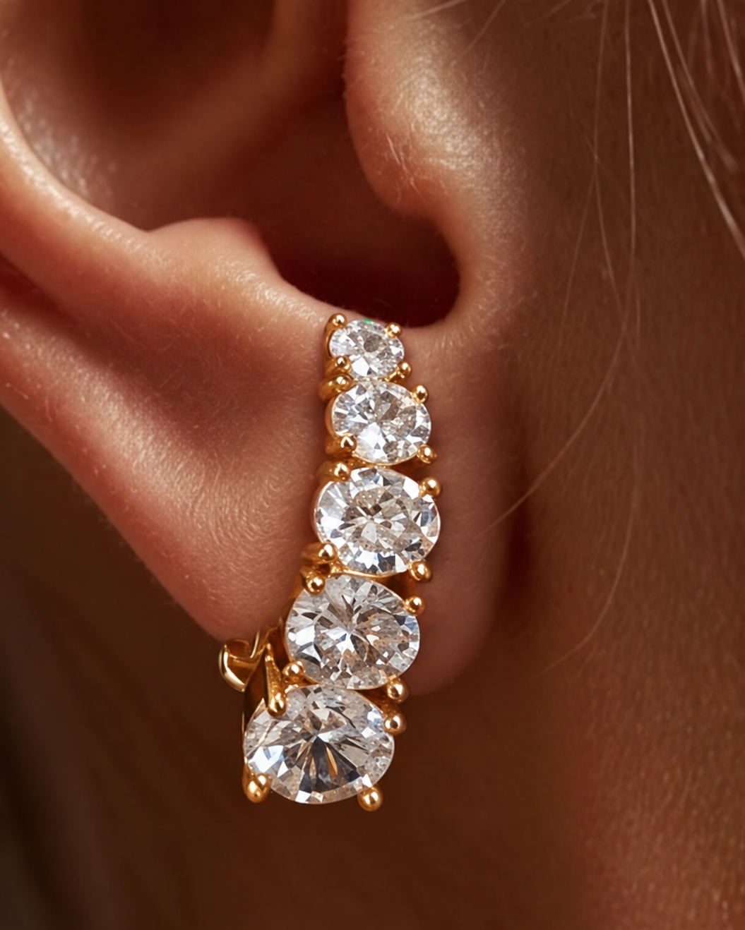 Brinco ear hook dourado com três pedras redondas transparentes