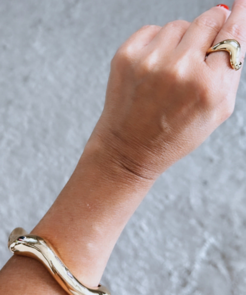 Bracelete dourado ondulado com abertura, detalhe no pulso e mão