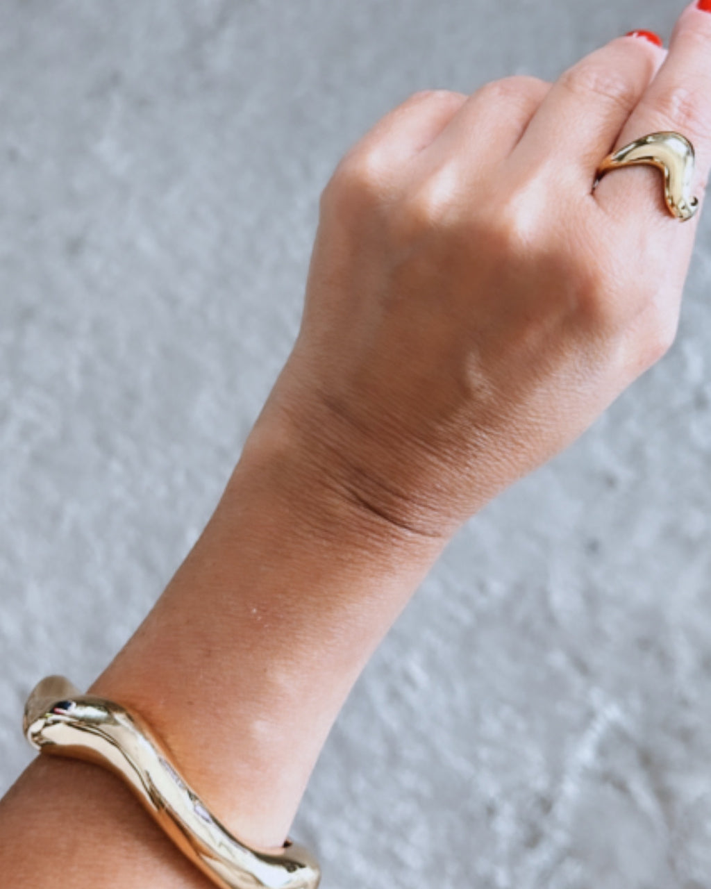 Bracelete dourado ondulado com abertura, detalhe no pulso e mão