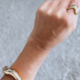 Bracelete dourado ondulado com abertura, detalhe no pulso e mão