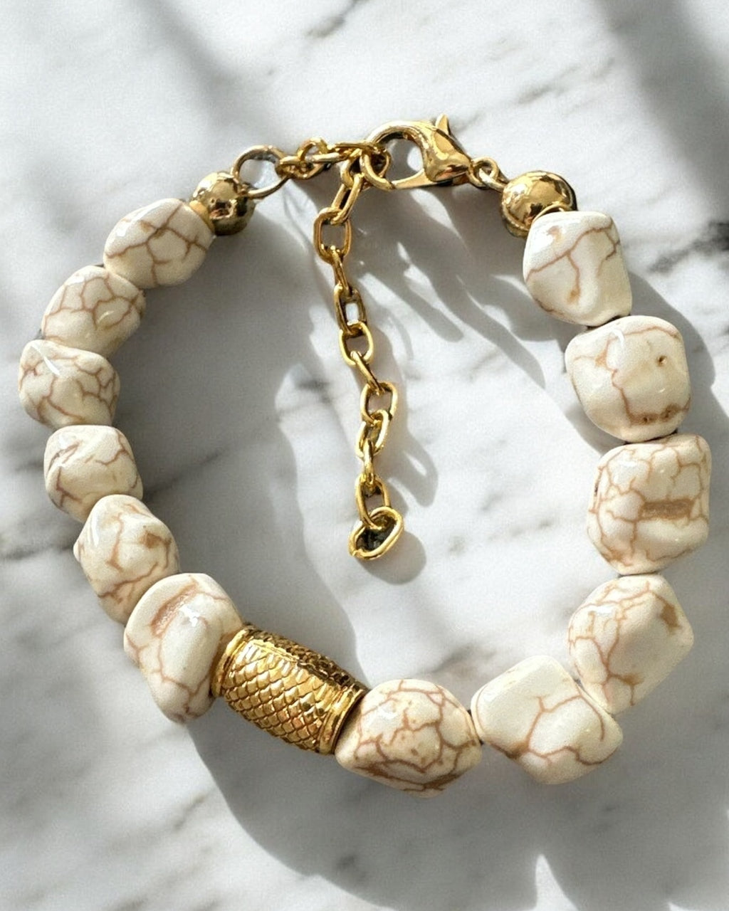 Pulseira de contas brancas com detalhe dourado texturizado e fecho em corrente.