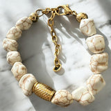 Pulseira de contas brancas com detalhe dourado texturizado e fecho em corrente.