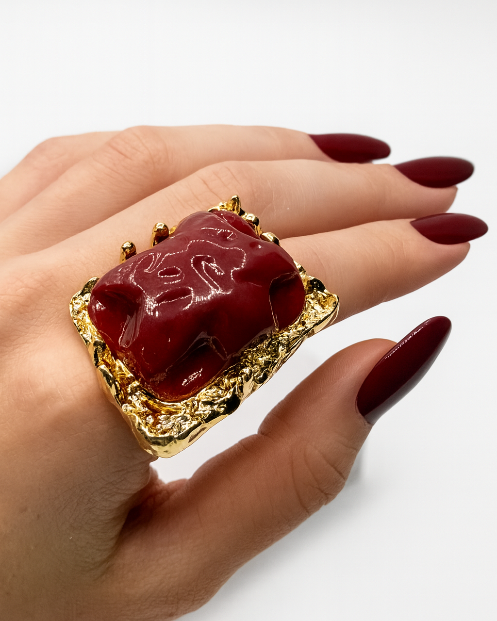 Anel Ursula com pedra vermelha escura em aro dourado com borda trabalhada