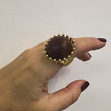 Anel Bia dourado com pedra oval escura e borda de pequenas esferas douradas