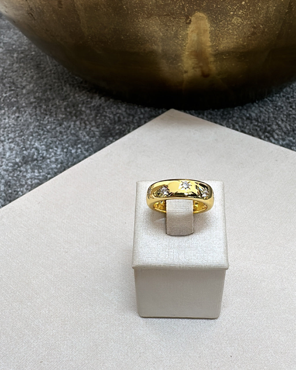 Anel dourado com pedras no topo e detalhe central retangular