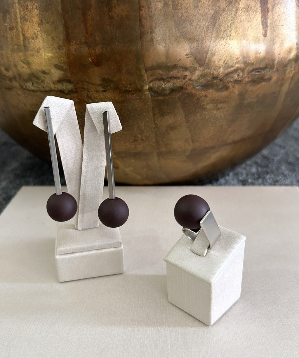 Brincos de haste reta com esferas marrom, metal dourado, exibidos em suporte branco