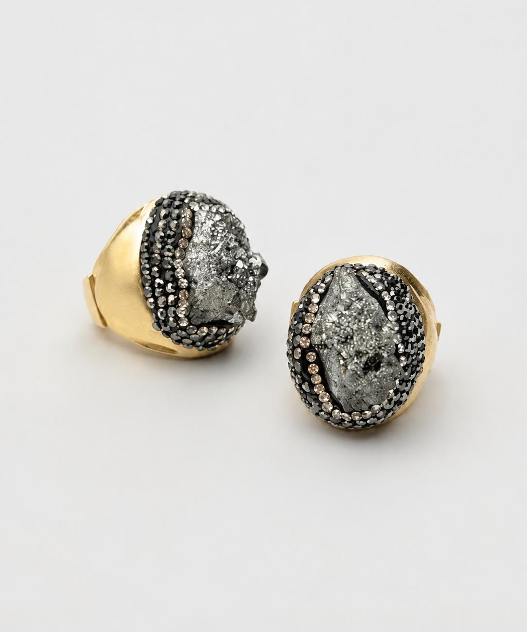Par de anéis Fira com aro dourado e pedra cinza escura oval com detalhes cravejados