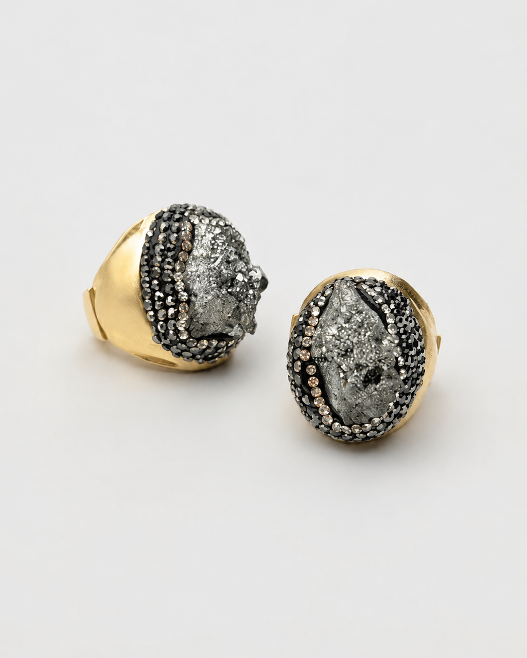 Par de anéis Fira com aro dourado e pedra cinza escura oval com detalhes cravejados