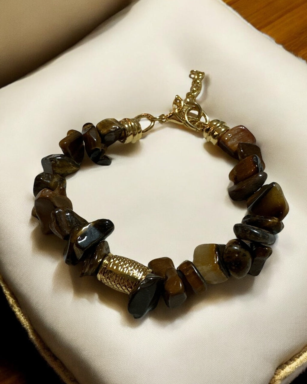 Pulseira de contas marrons escuras com fecho dourado e peça central texturizada.