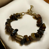 Pulseira de contas marrons escuras com fecho dourado e peça central texturizada.