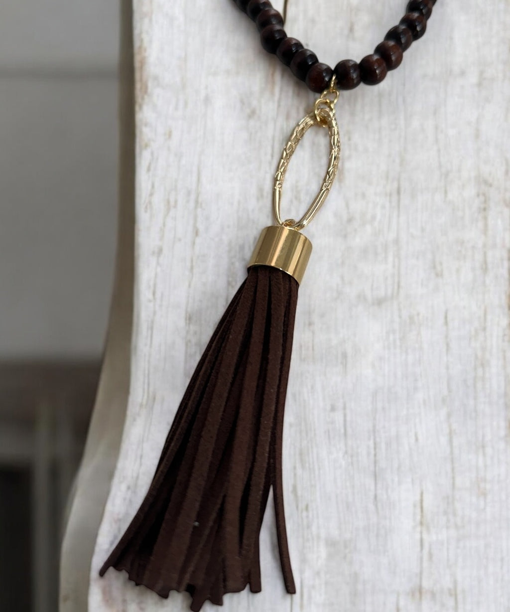 Colar boho com contas escuras e pingente de franja marrom preso por argola dourada