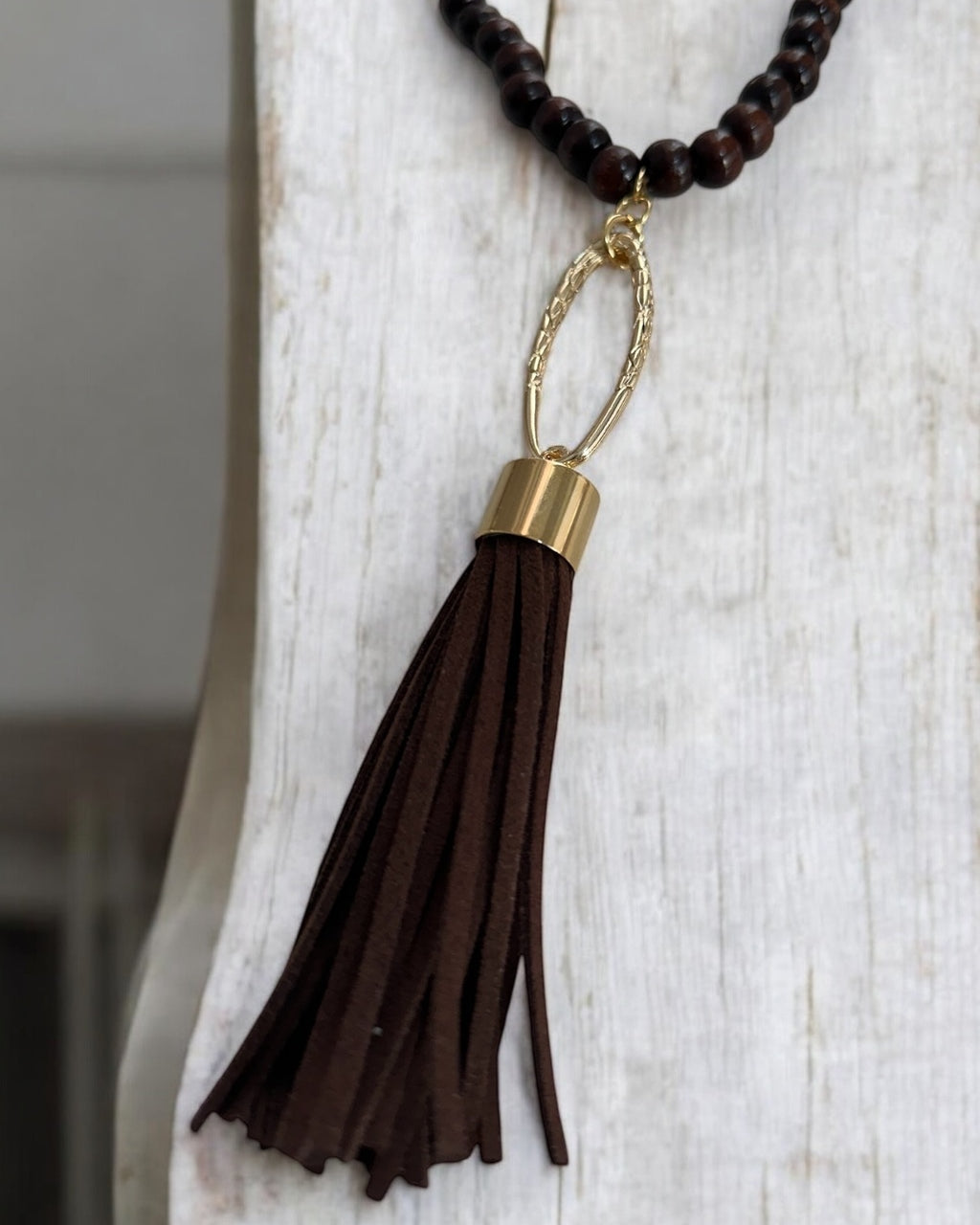 Colar boho com contas escuras e pingente de franja marrom preso por argola dourada