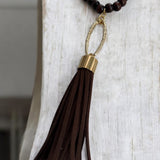 Colar boho com contas escuras e pingente de franja marrom preso por argola dourada