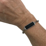 Pulseira com placa retangular escura e corrente prateada com detalhes