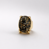 Anel oval com pedra escura salpicada de dourado em aro dourado