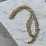Colar de contas bege com pingente de chifre dourado e fecho metálico