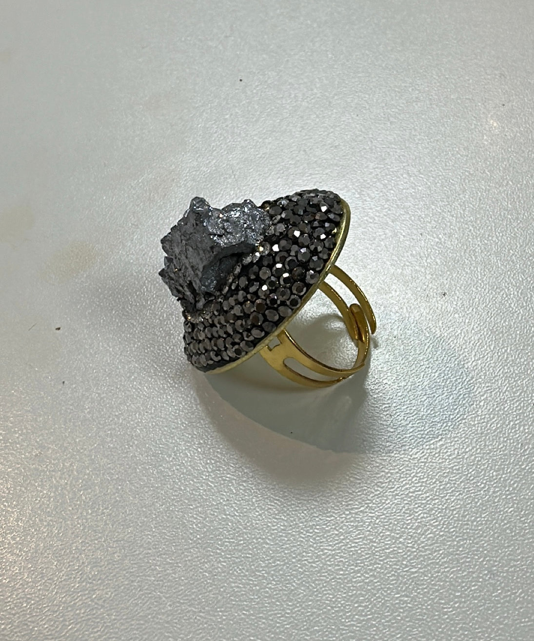 Anel maxi oval com pedras pretas e cinzas; faixa dourada visível por baixo