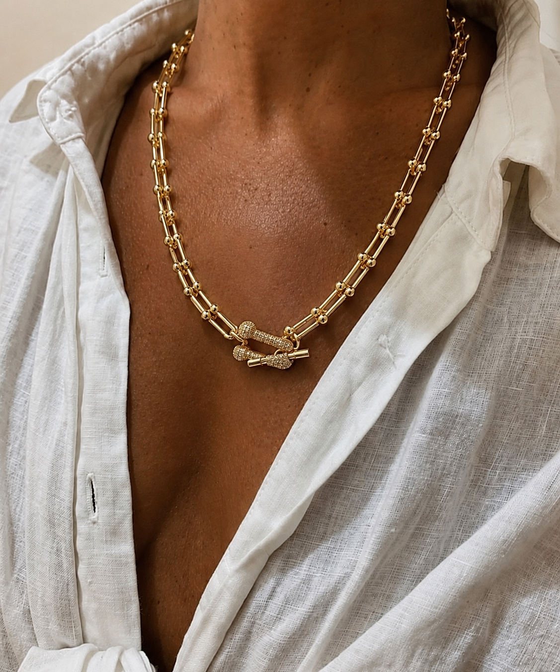 Colar dourado com elos retangulares e pingente central com cristais, fecho discreto