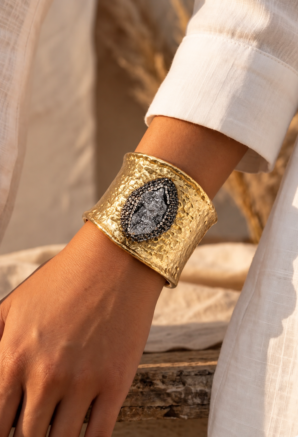 Bracelete Fira largo dourado com pedra oval cinza-escura, usado no pulso