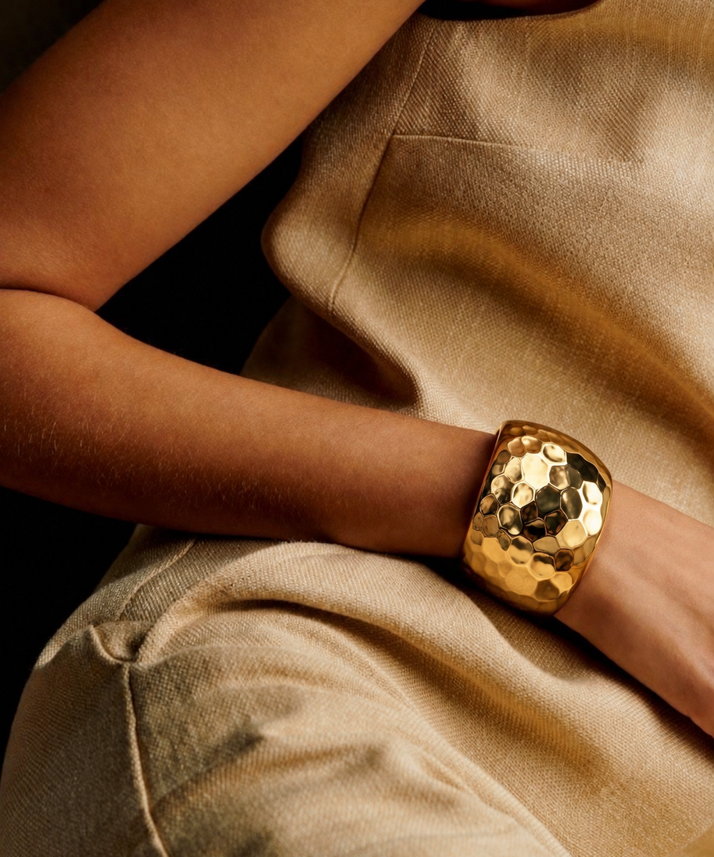 Bracelete dourado espelhado em mão, textura martelada, sobre tecido bege