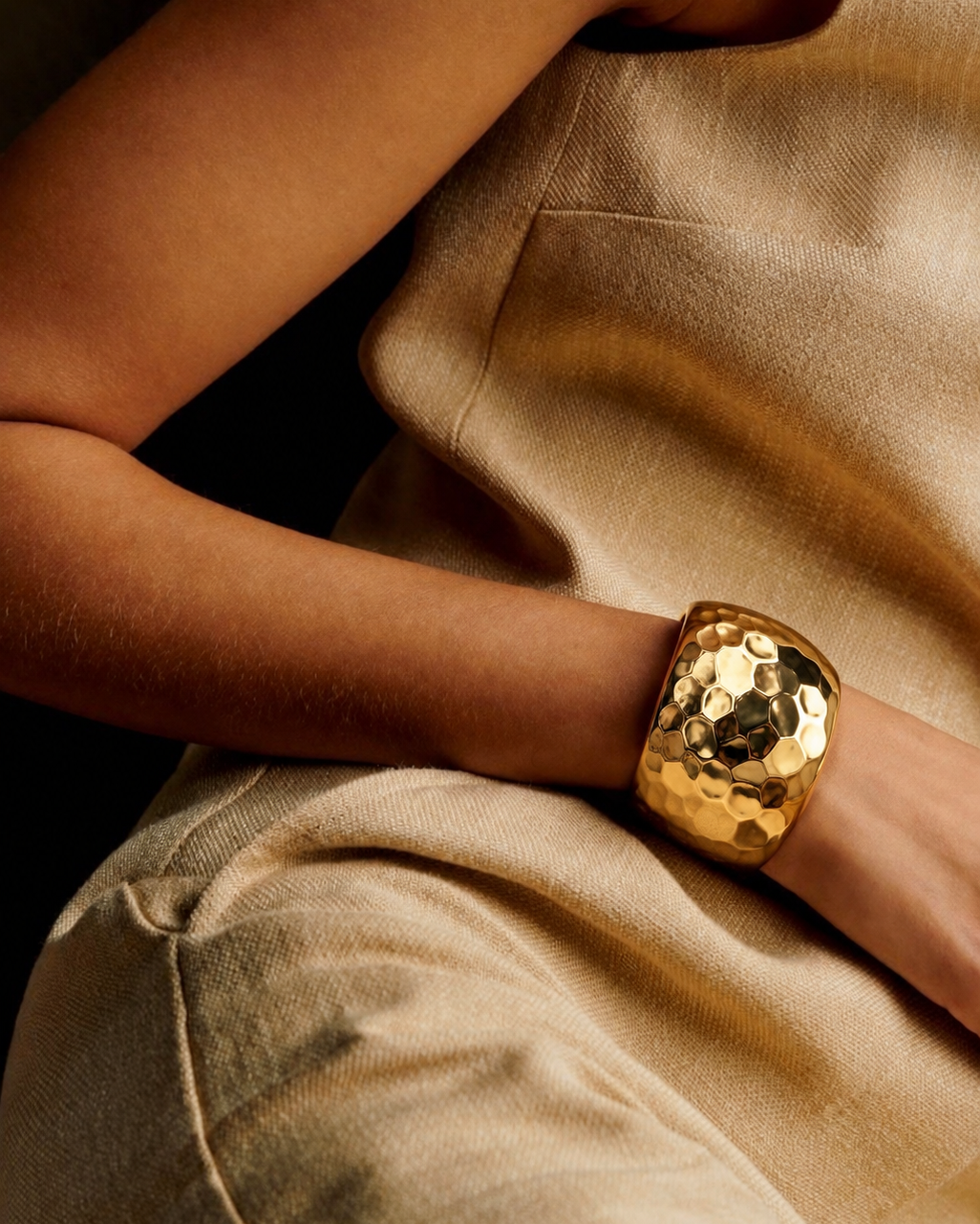 Bracelete dourado espelhado em mão, textura martelada, sobre tecido bege