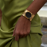 Bracelete largo dourado com base texturizada e pedra oval preta ao centro