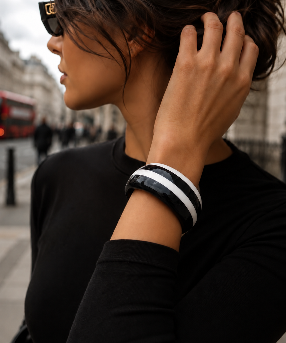 Pulseira no pulso com elos pretos e lisos com faixas brancas, estilo bangle.