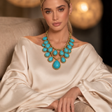 Colar dourado com pedras turquesa na gola, formato oval e gota, usado com vestido claro