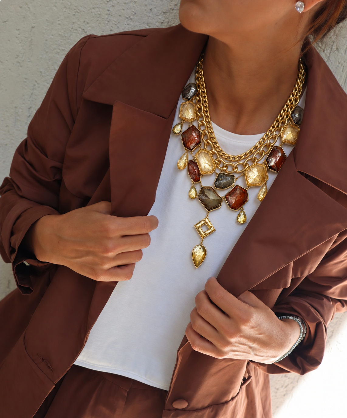Colar dourado de corrente com pingentes coloridos, usado com blusa branca e blazer marrom