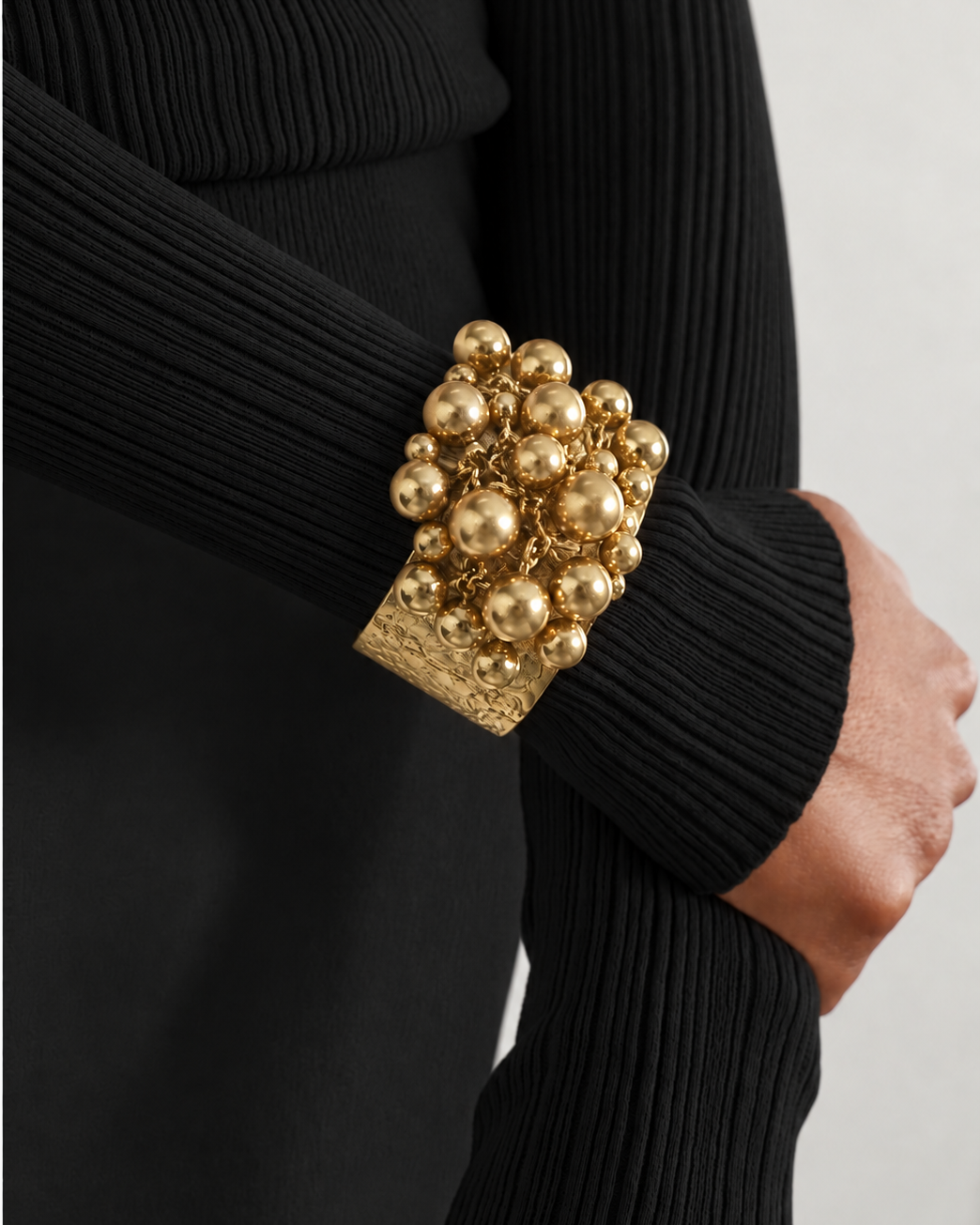 Pulseira Valina dourada com contas esféricas e placa texturizada, usada no punho